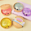 A collection of squishy glitter steamed buns and a sparkly purple fidget toy displayed on a pink book.