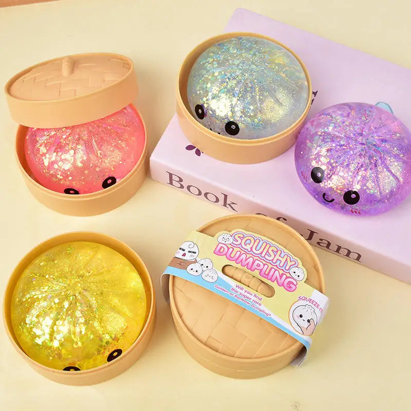 A collection of squishy glitter steamed buns and a sparkly purple fidget toy displayed on a pink book.