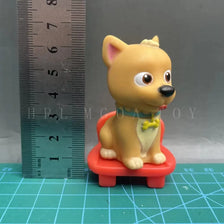 A yellow cartoon figurine resembling a dog wearing a collar, sitting on a red stool, next to a ruler.