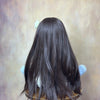 A dark brown, long-haired silicone baby doll with white accents is displayed on a stand.