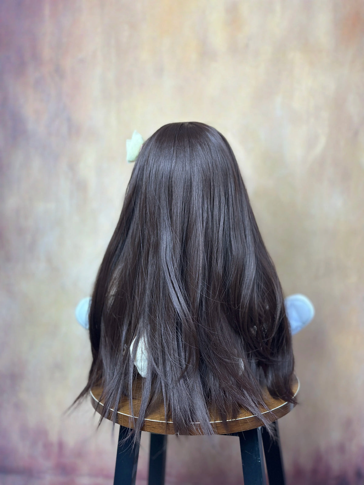 A dark brown, long-haired silicone baby doll with white accents is displayed on a stand.