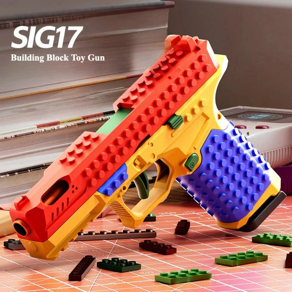 An orange and yellow building block toy gun is displayed on a red surface with various green and brown building blocks.