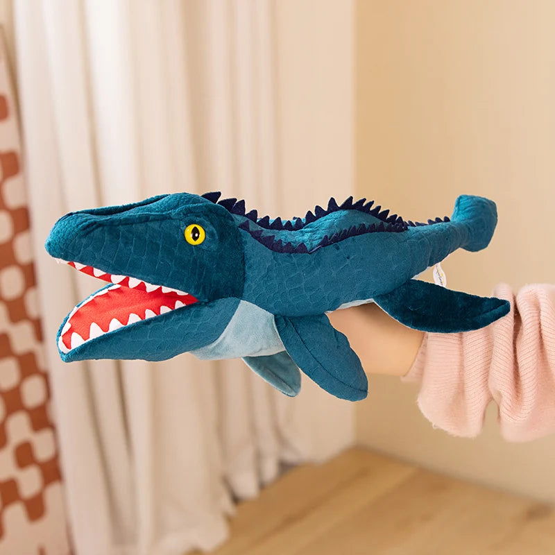 Marionnette en peluche de dinosaure teinté de bleu sarcelle avec des yeux jaunes et des dents blanches tenue par une personne