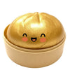 A golden, round squishy toy shaped like a dumpling with cute facial features resting in a light beige container.