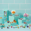 A collection of Mini Brands Mystery Balls and related items displayed on a light blue surface against a teal tiled background