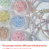 A collection of 300 loose individual glass beads in various colors including pink, blue, and gold scattered on a white surfac