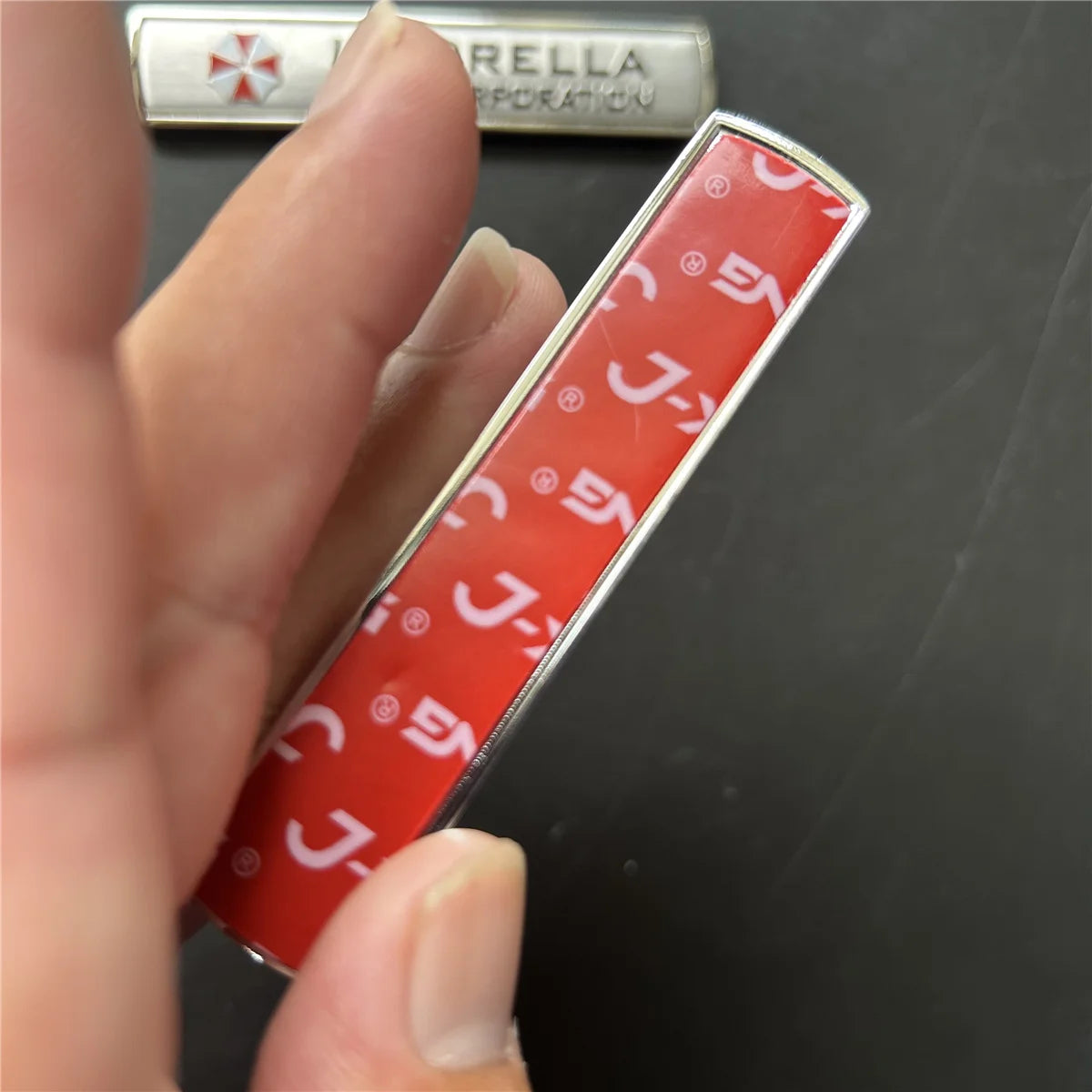 A hand holds a red and white emblem badge for Umbrella Corporation.