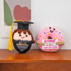 A handmade crochet graduation gift featuring a black felted owl with a graduation cap and a pink donut with an inspirational 