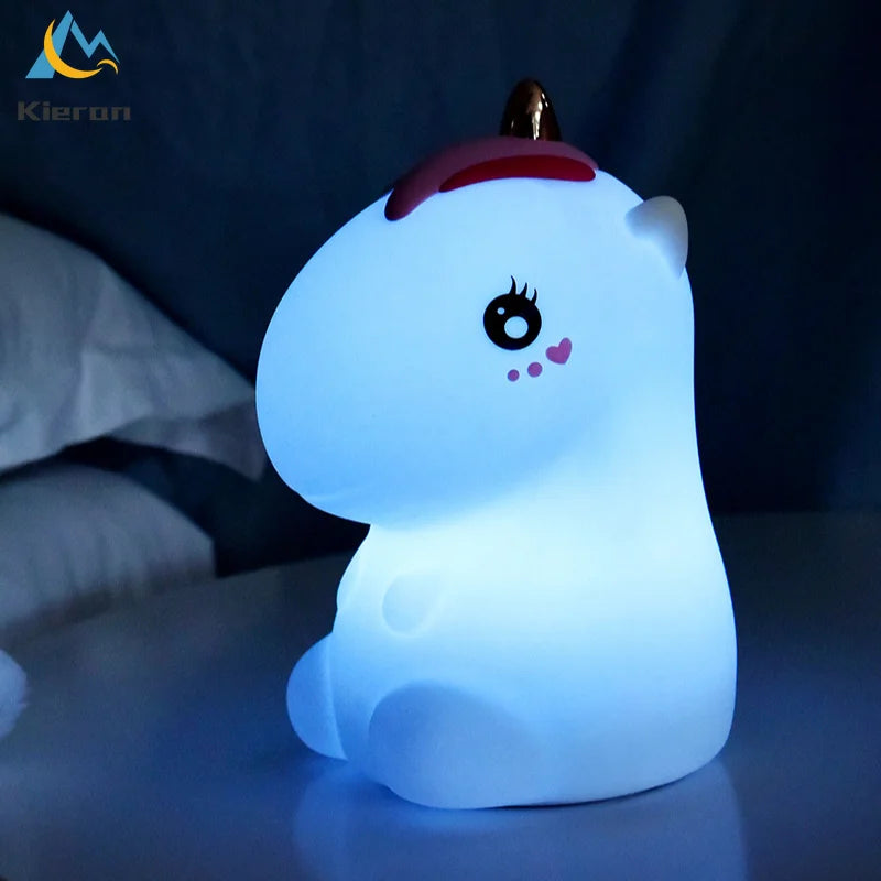 A white unicorn LED night light with a pink horn and touch control resting on a surface.