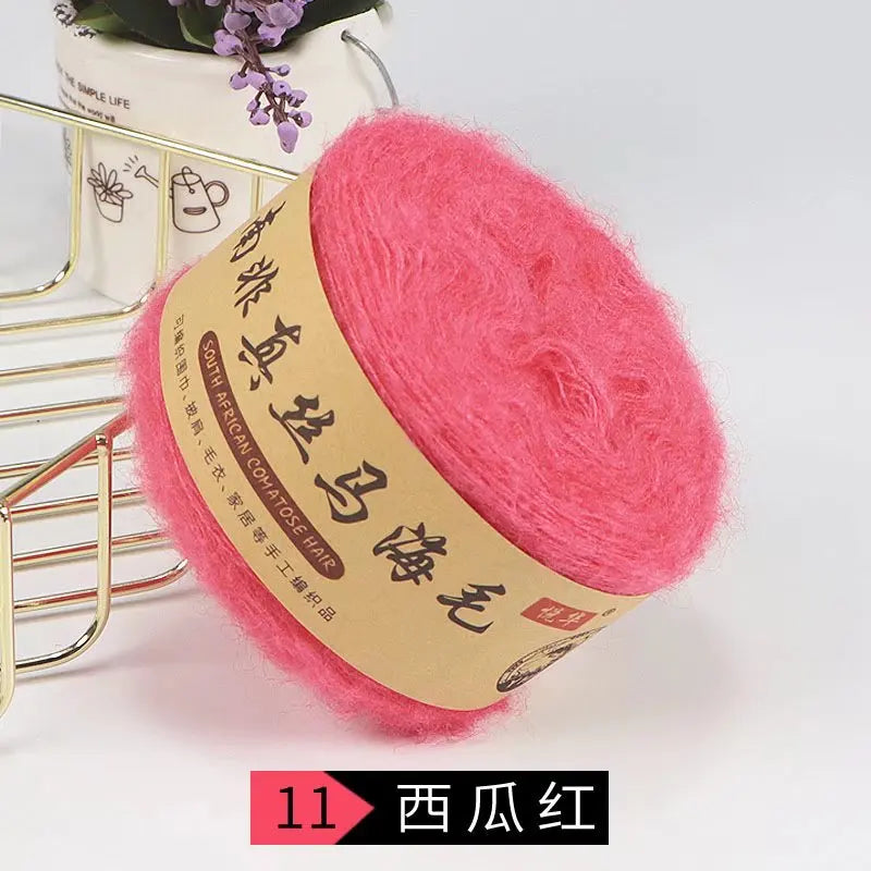 A ball of bright pink silk mohair blended yarn for knitting, displayed next to a gold wire rack.