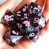 A hand holds a set of pink and green polyhedral dice made from handmade resin
