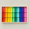 A wooden tray filled with colorful rainbow acrylic building blocks arranged in a grid.