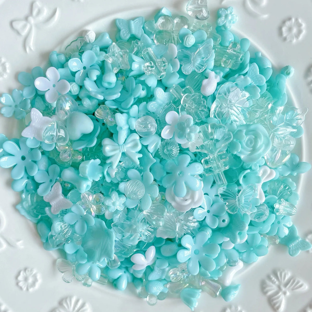 A pile of light blue and clear acrylic bow and flower beads for DIY jewelry making