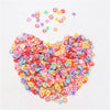 A heart shape made of colorful polymer clay flower charms scattered on a white background.