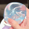 A hand holds a translucent, silicone fidget ball shaped like a coconut, displaying soft blue and pink swirling colors.