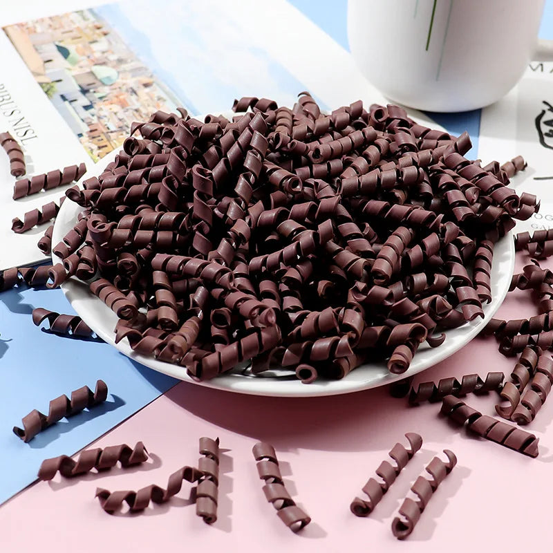 A pile of dark brown polymer clay marshmallow charms for DIY crafts is displayed on a white plate.