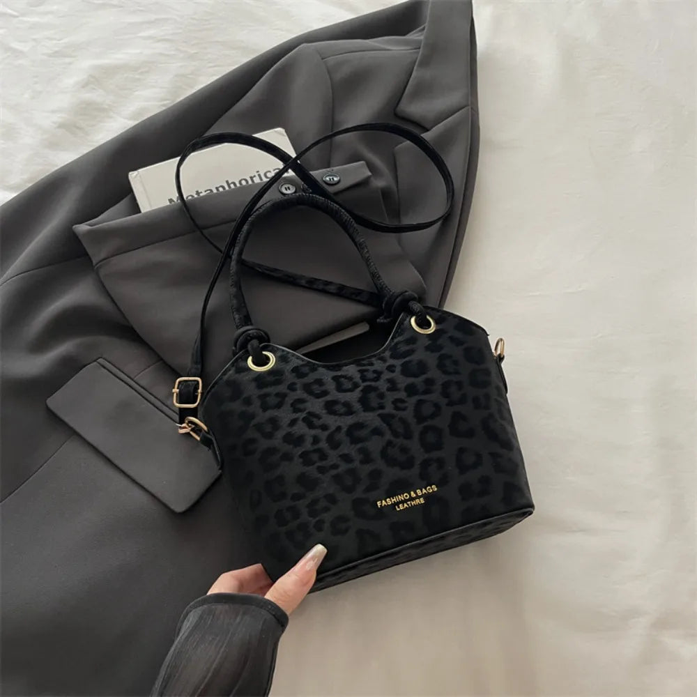 A black leopard print canvas tote bag with gold hardware is shown resting on a gray blazer.