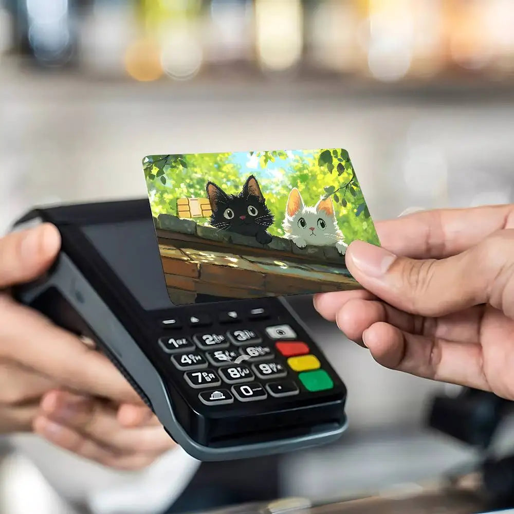 A hand holds a black card with a cat design against a dark electronic device.