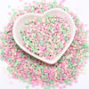 A heart-shaped dish filled with pink and green polymer clay sprinkles scattered on a white background.