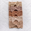 A stack of five beige and tan knitted fabric bow baby headbands.