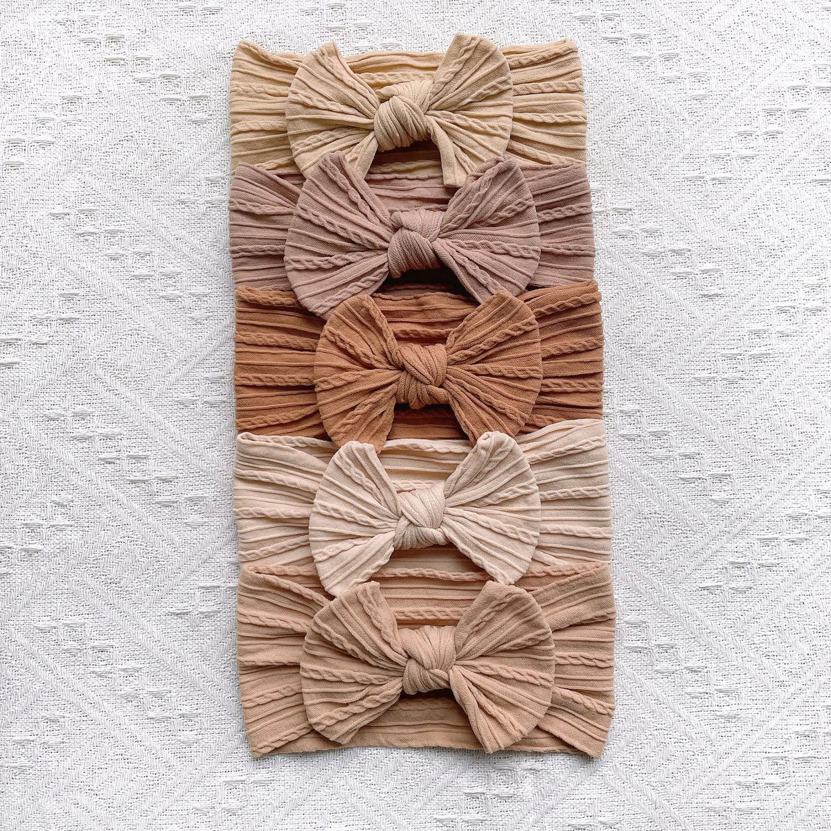A stack of five beige and tan knitted fabric bow baby headbands.
