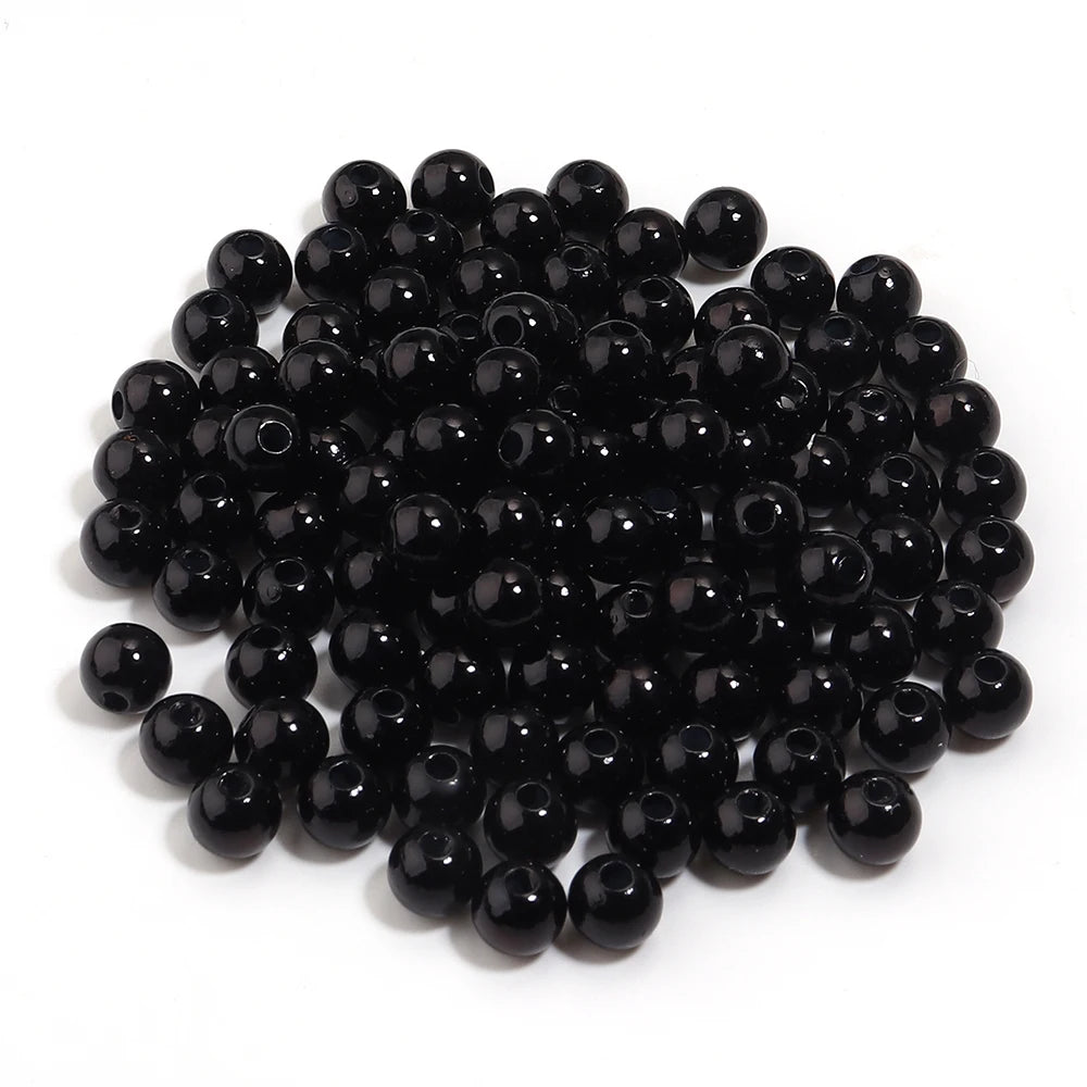 A pile of small, round, black imitation pearl beads for jewelry making.