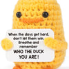 A yellow crochet duck plush toy with a white sign featuring an inspirational message.