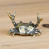 A brass crab figurine statue with detailed claws resting on a wooden surface.