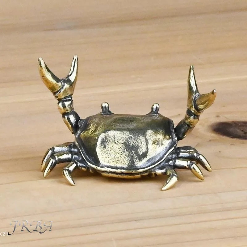 A brass crab figurine statue with detailed claws resting on a wooden surface.