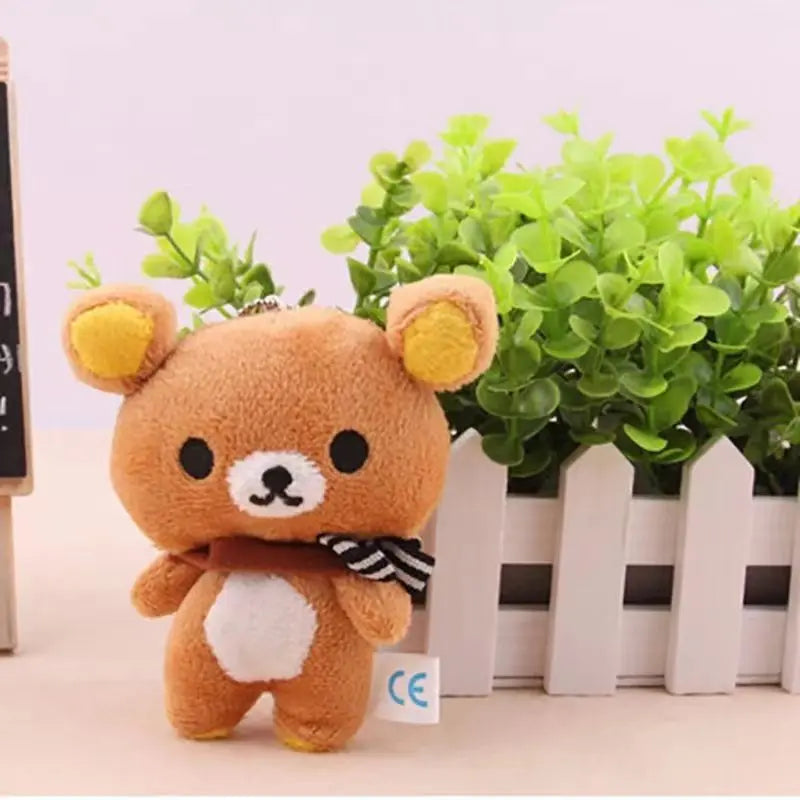 A fluffy brown Kawaii Rilakkuma Strawberry Bear plush toy standing in front of green foliage.