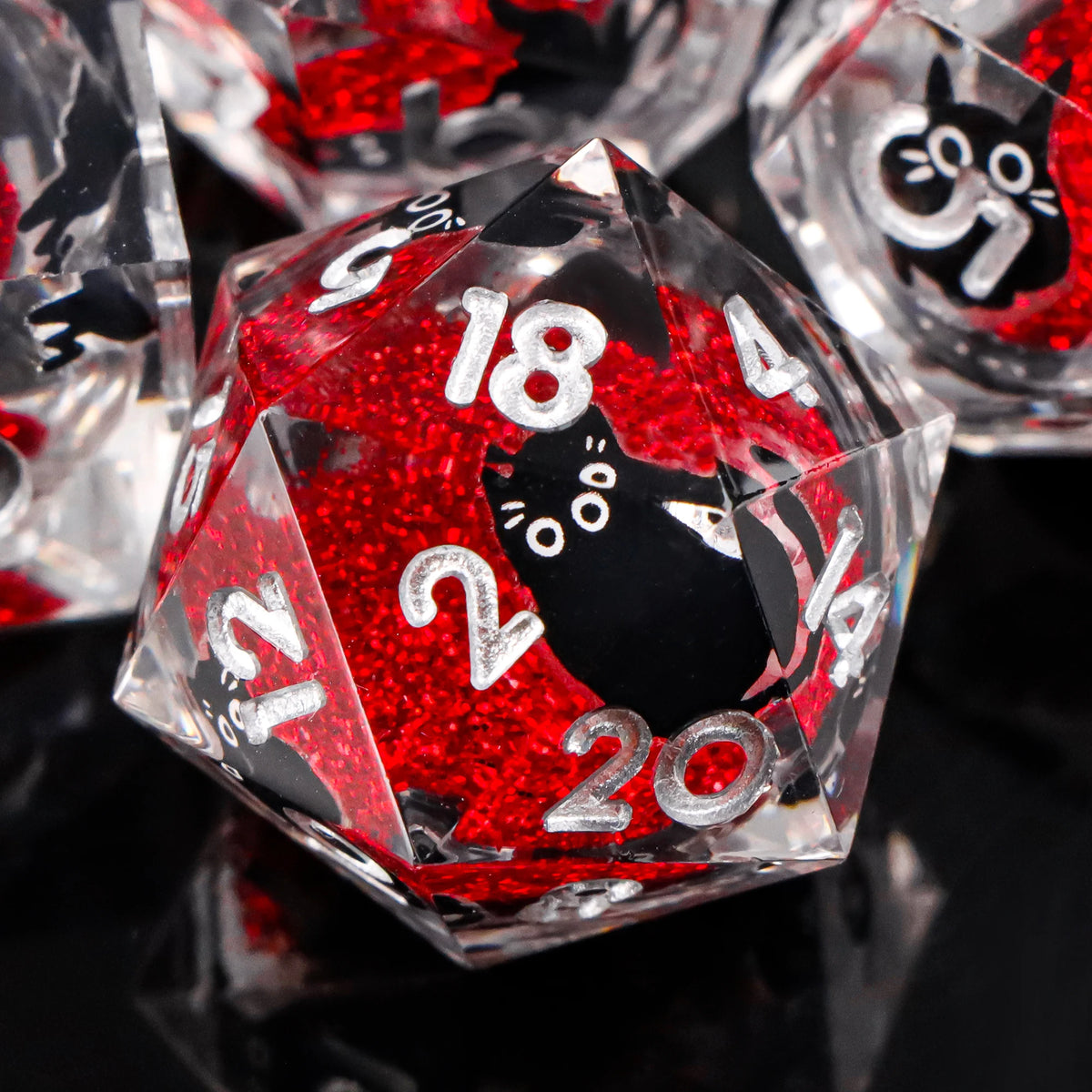 A close-up of red glitter resin dice shaped like pyramids and dodecahedrons, featuring black cat designs.