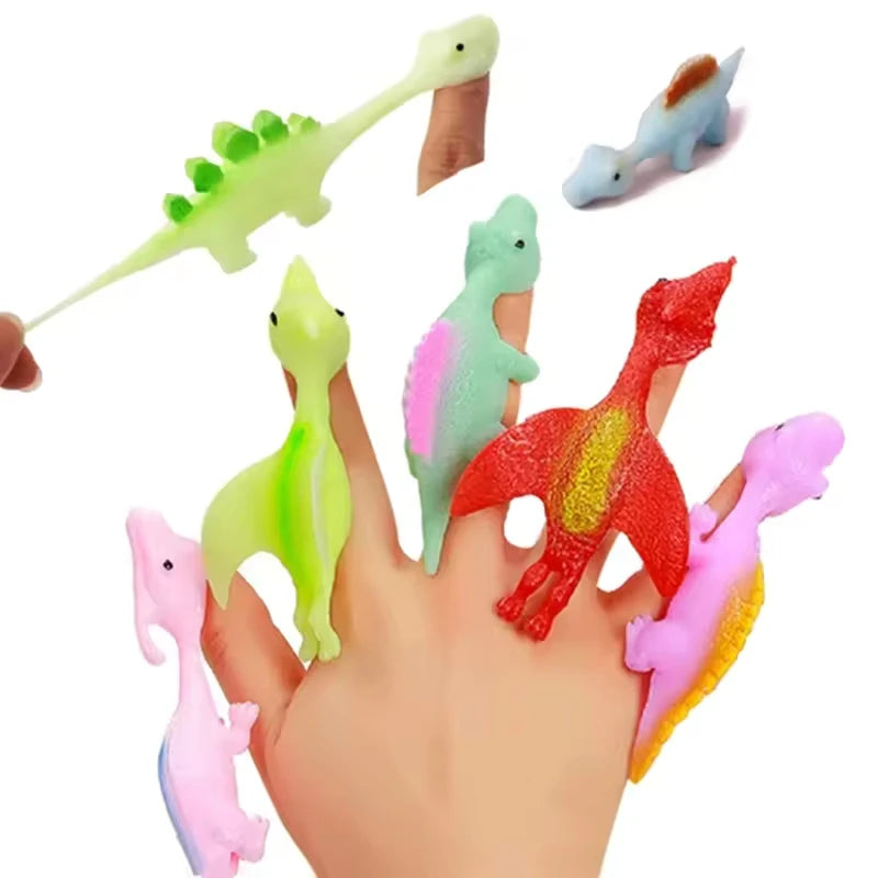 A hand holds a set of colorful rubber dinosaur slingshot toys, including green, blue, and red dinosaurs.