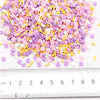 A pile of colorful polymer clay flower charms in shades of pink, purple, and yellow scattered on a white surface next to a ru