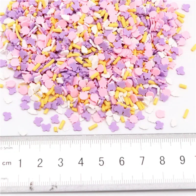 A pile of colorful polymer clay flower charms in shades of pink, purple, and yellow scattered on a white surface next to a ru