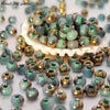 A pile of vibrant round beads in various shades of green and gold for jewelry making