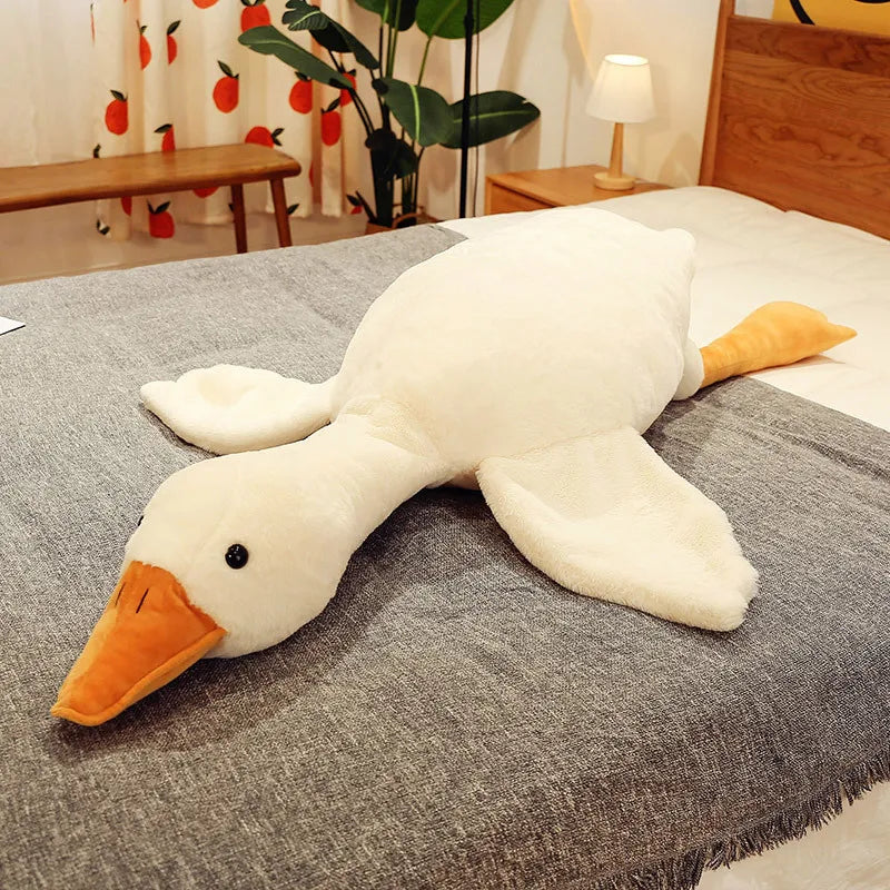 A large, white kawaii goose plush pillow with an orange beak resting on a gray fabric surface.