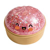 A pink, squishy stress relief toy shaped like a smiling dumpling face with glitter accents.