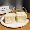 Two white cheese cube stress balls placed on a white plate next to some boxed items.