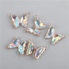 Several iridescent crystal butterfly charm beads in gold-toned metal are displayed on a gray background.
