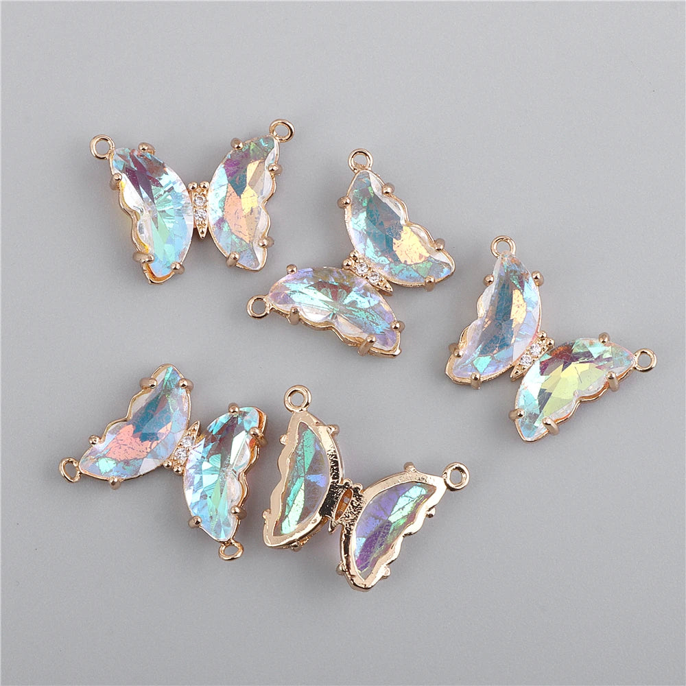 Several iridescent crystal butterfly charm beads in gold-toned metal are displayed on a gray background.