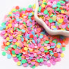 A pile of colorful polymer clay sprinkles in various shades of pink, orange, yellow, and green, with some spilling into a whi