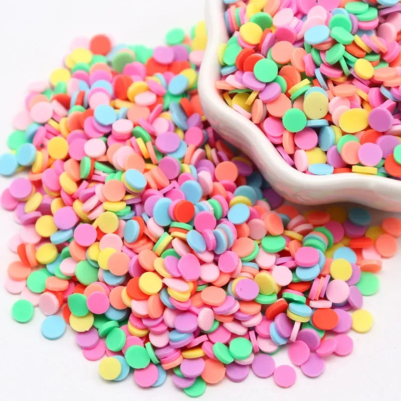 A pile of colorful polymer clay sprinkles in various shades of pink, orange, yellow, and green, with a scoop visible.