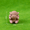 A small, light brown resin figurine of a hippo in a sitting pose, photographed on green grass.