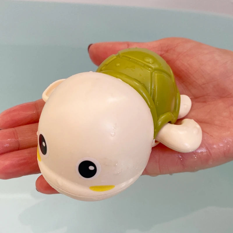 A hand holds a light yellow bath time basketball hoop set with a green ball and a white ball.