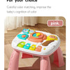 A pink musical baby piano playmat with a light-up keyboard and hanging toys is shown on a wooden floor.