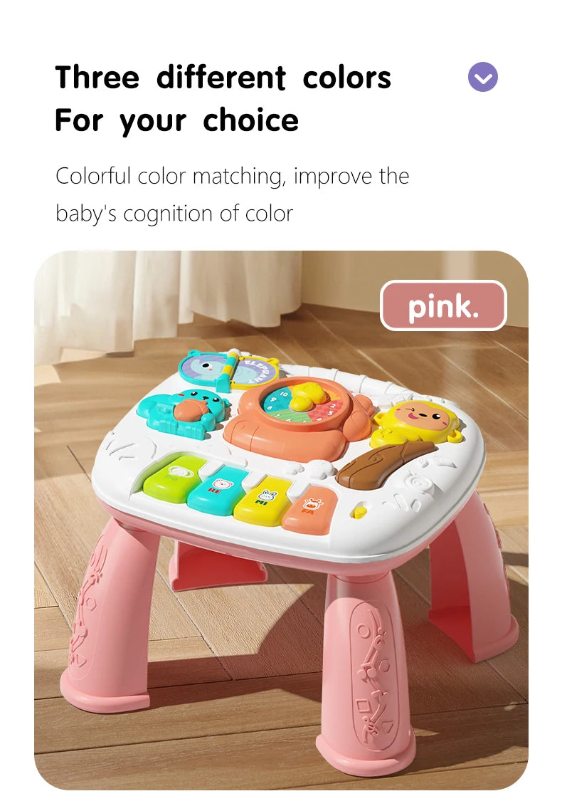 A pink musical baby piano playmat with a light-up keyboard and hanging toys is shown on a wooden floor.