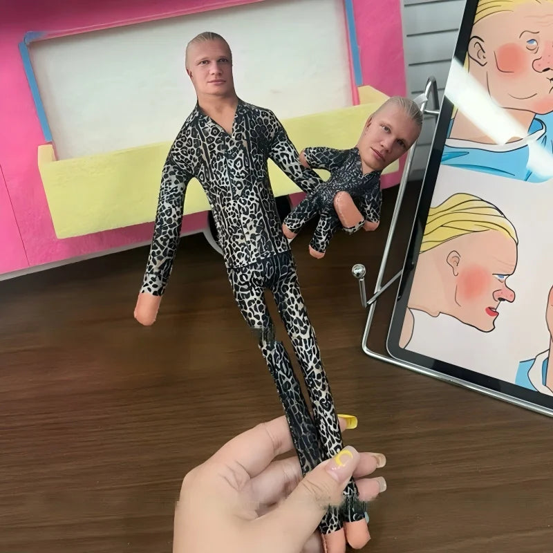 A man is holding a realistic stuffed doll of Erling Haaland with flexible joints.