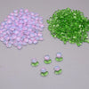 A pile of pink and purple glass beads next to a pile of green glass beads.
