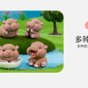 Three cute mini hippo resin figurines sitting on green grass with a tree in the background.