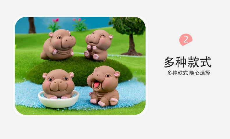 Three cute mini hippo resin figurines sitting on green grass with a tree in the background.